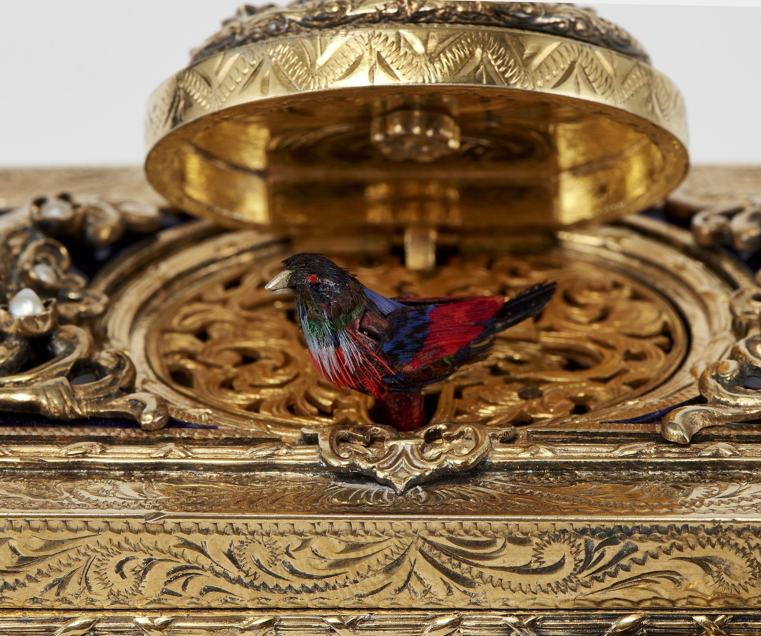 Boîte à oiseau chanteur à riche décor de volutes, gravée et ajourée, incrustée de perles et cabochons d'émeraudes et grenats